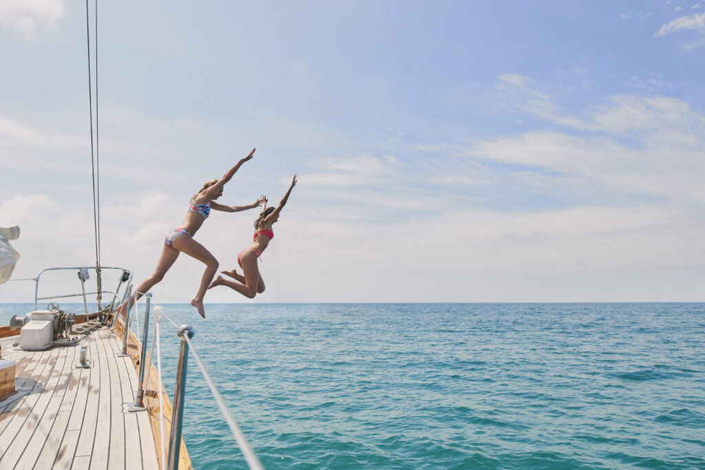 two-girls-jumping-off-boat-yacht-into-ocean-water